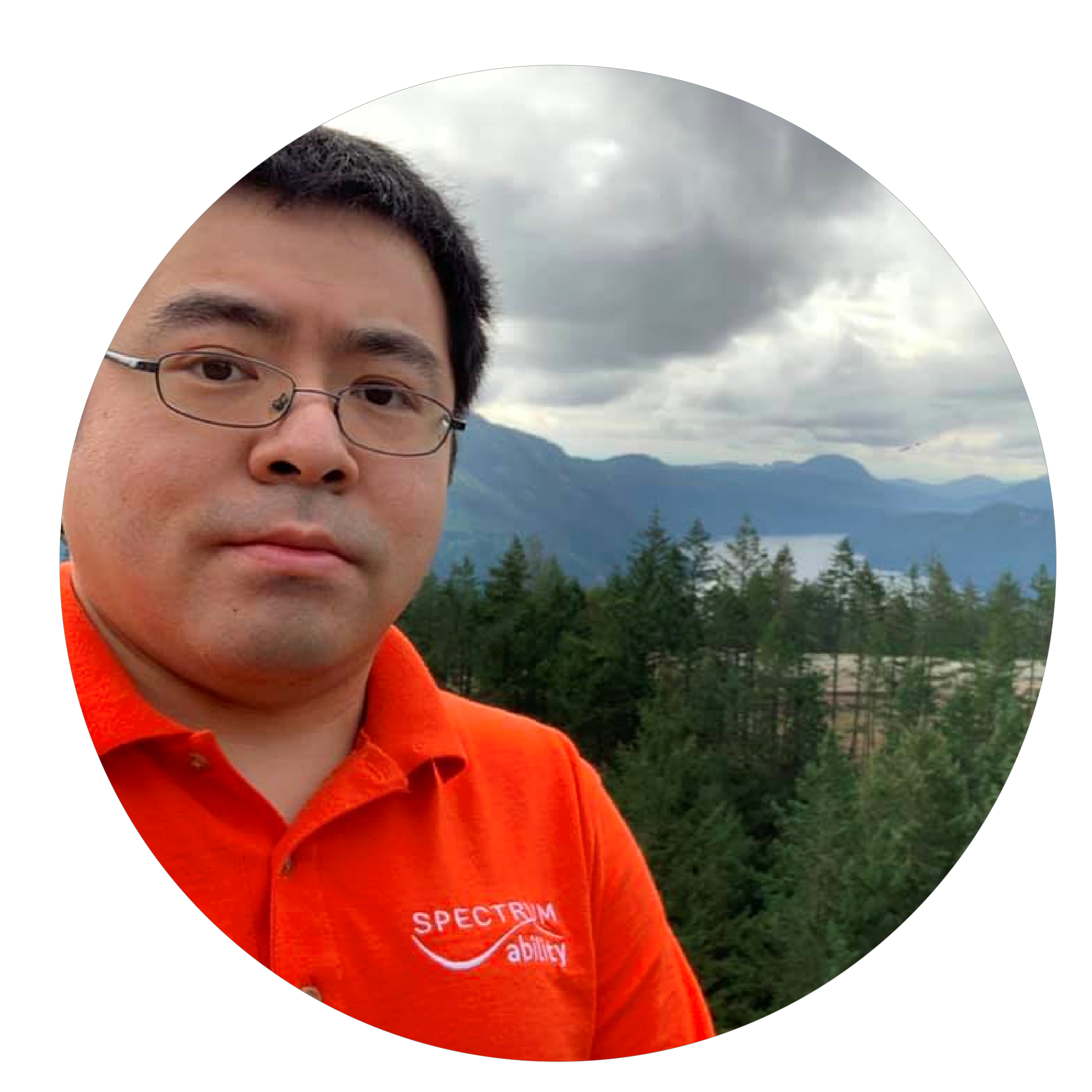 A man in glasses and a bright orange polo shirt with trees and mountains in background