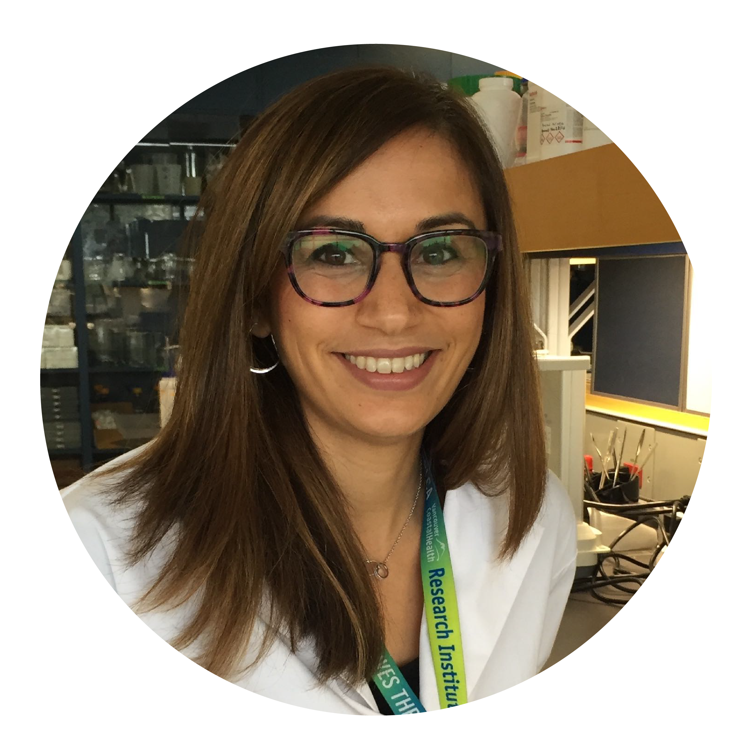 A woman in a white coat, green lanyard and brown glasses with medium lenght brown hair