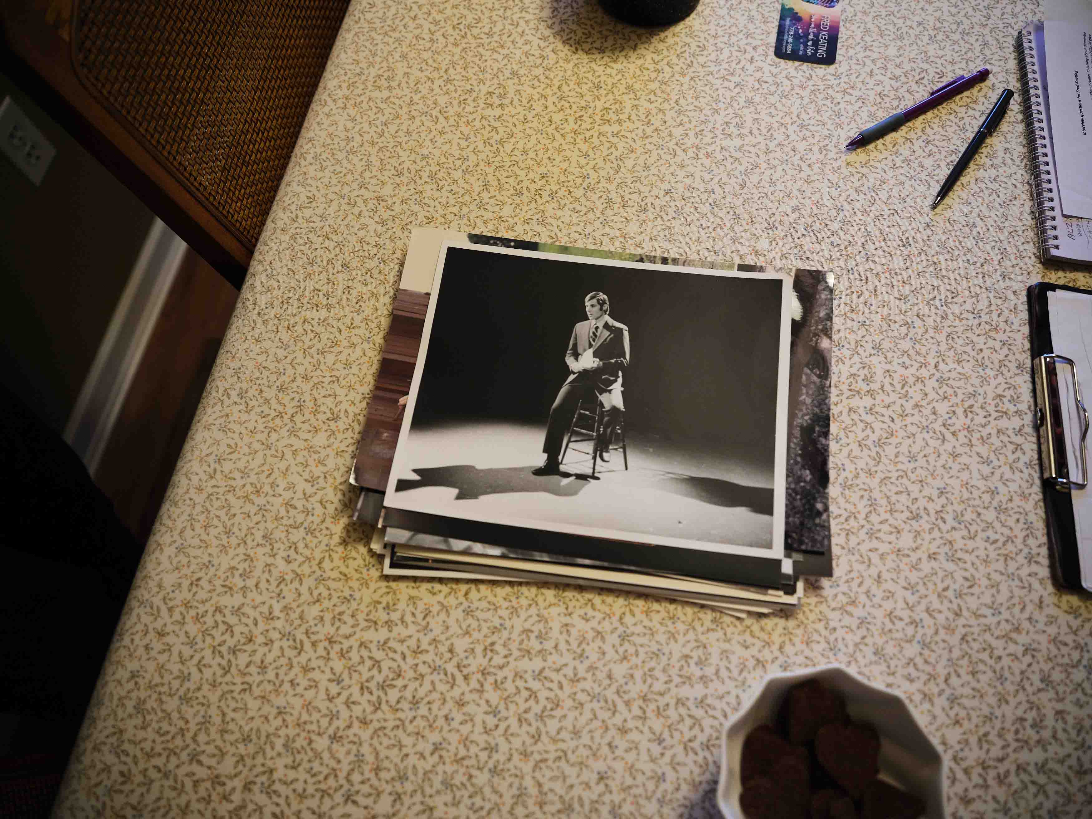 A stack of old photographs on a table, topped with a black-and-white photo of a man performing on stage.