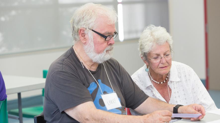 Woman leaning over man's shoulder as they read a slip of paper together.