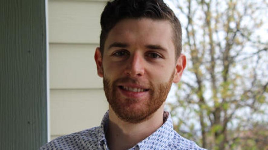 Nathan smiling in front of a house and trees.