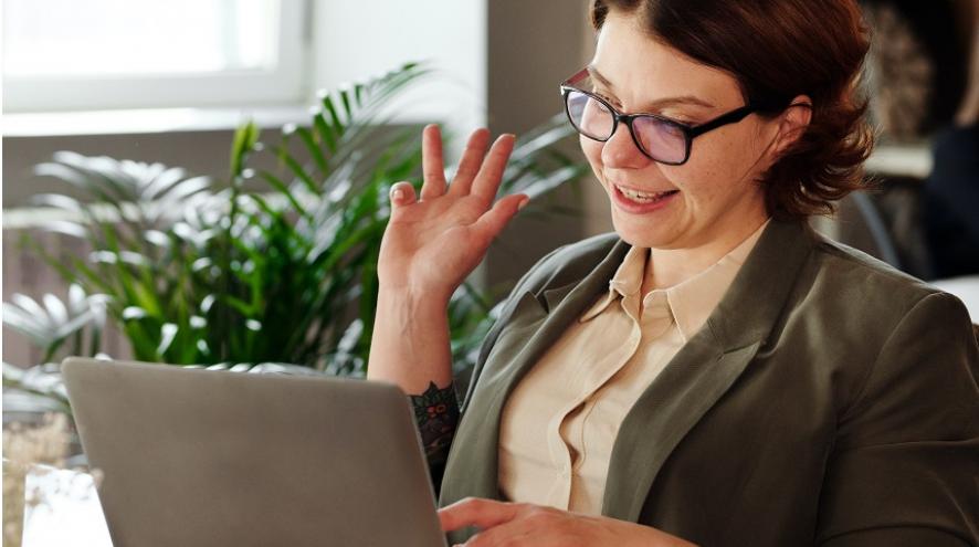 Woman waving in front of a laptop on a video call.