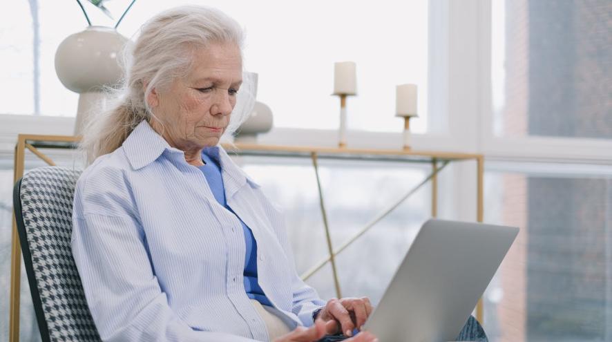 An older adult woman in striped long sleeves typing on laptop