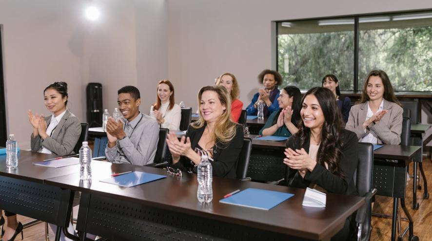 A group of people sit in a room, clapping and smiling following a presentation.