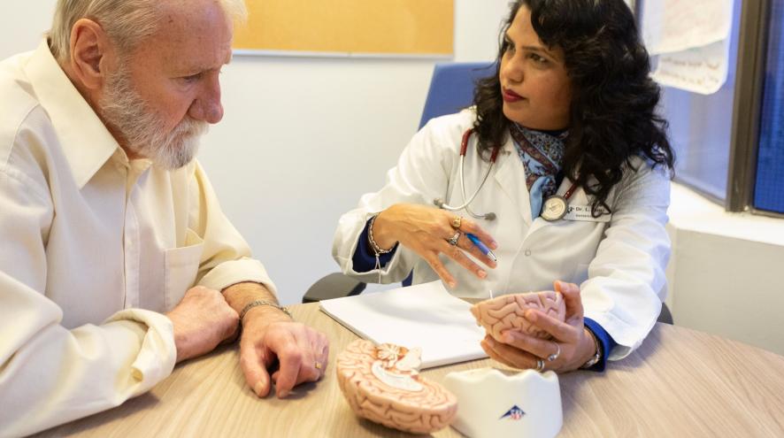 A man with a grey beard talking to a doctor with dark hair.