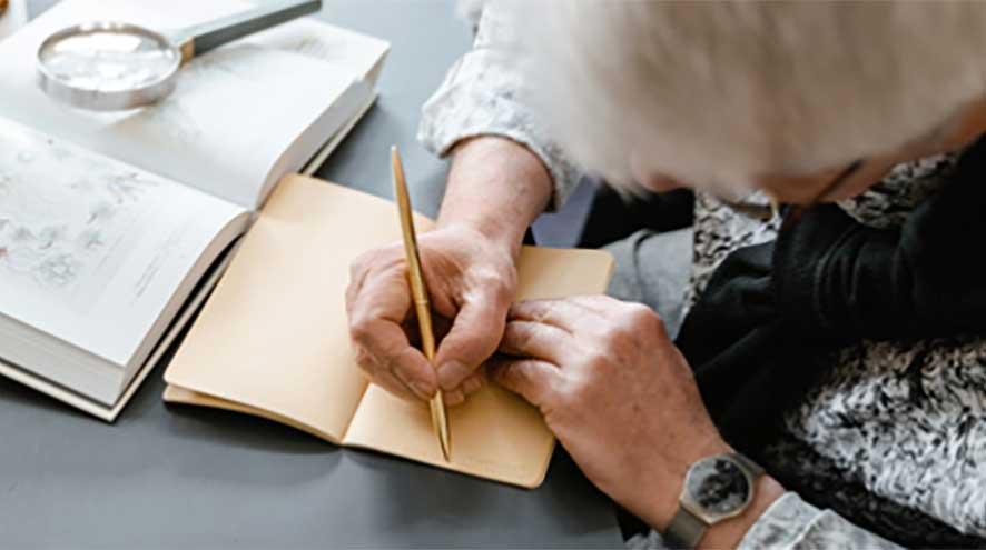 an elderly woman with her had down, writing in a journal