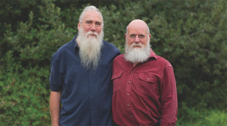 A male same-sex couple, arm in arm, in an outdoor portrait.