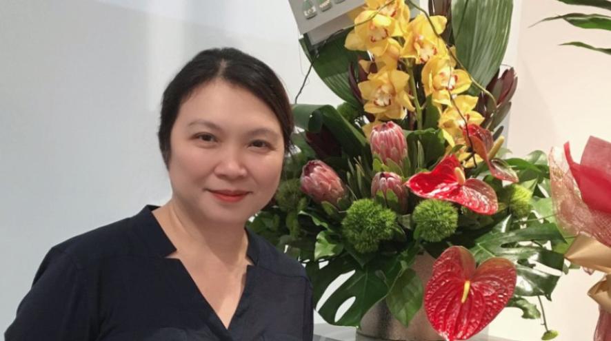 A woman wearing a black shirt stands against a very large, bright bouquet of flowers