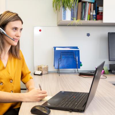 Helpline volunteer dressed in yellow at the laptop and listening intently.
