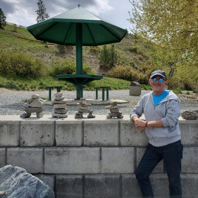 Craig wearing sunglasses and a hat, standing in front of a wall with stone stacking.