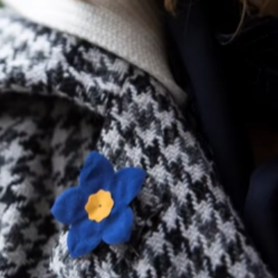 A person in a jacket wearing a blue forget me not pin