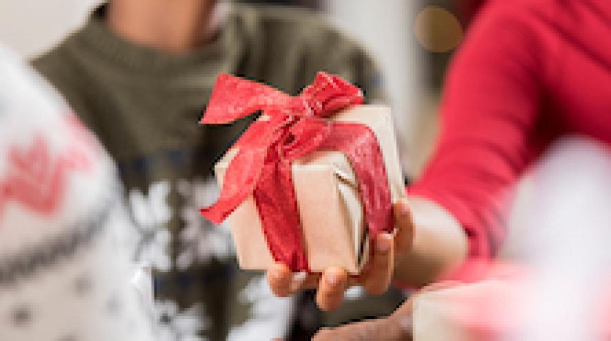 Person handing someone a small present with a red bow wrapped around it