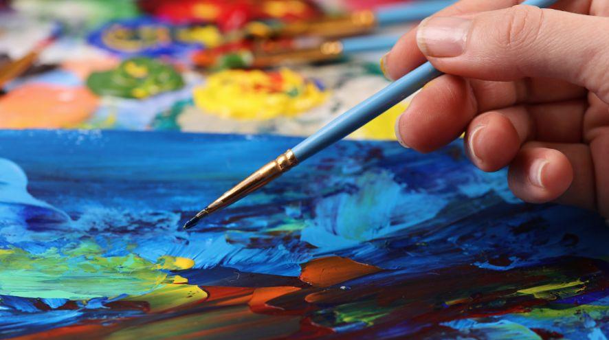 close up of hand holding paint brush on canvas