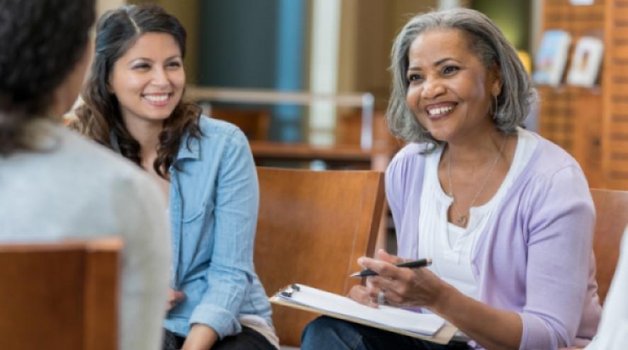 Smiling woman wearing purple with a clipboard at a support group