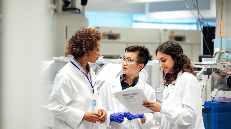 Three scientists in labcoats consult with each other